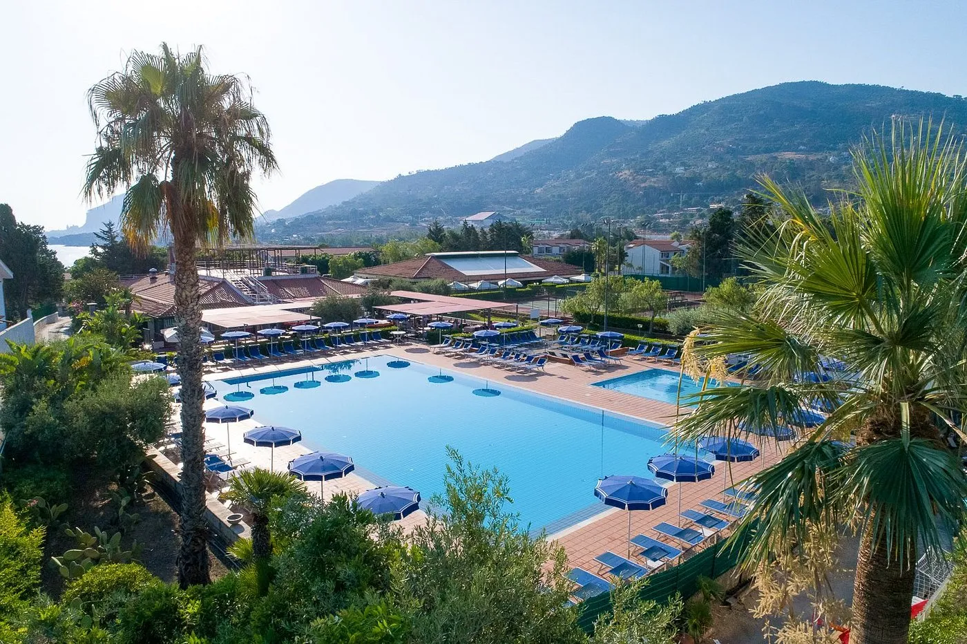 Veduta della piscina del resort tra palme con vista sul mare e colline