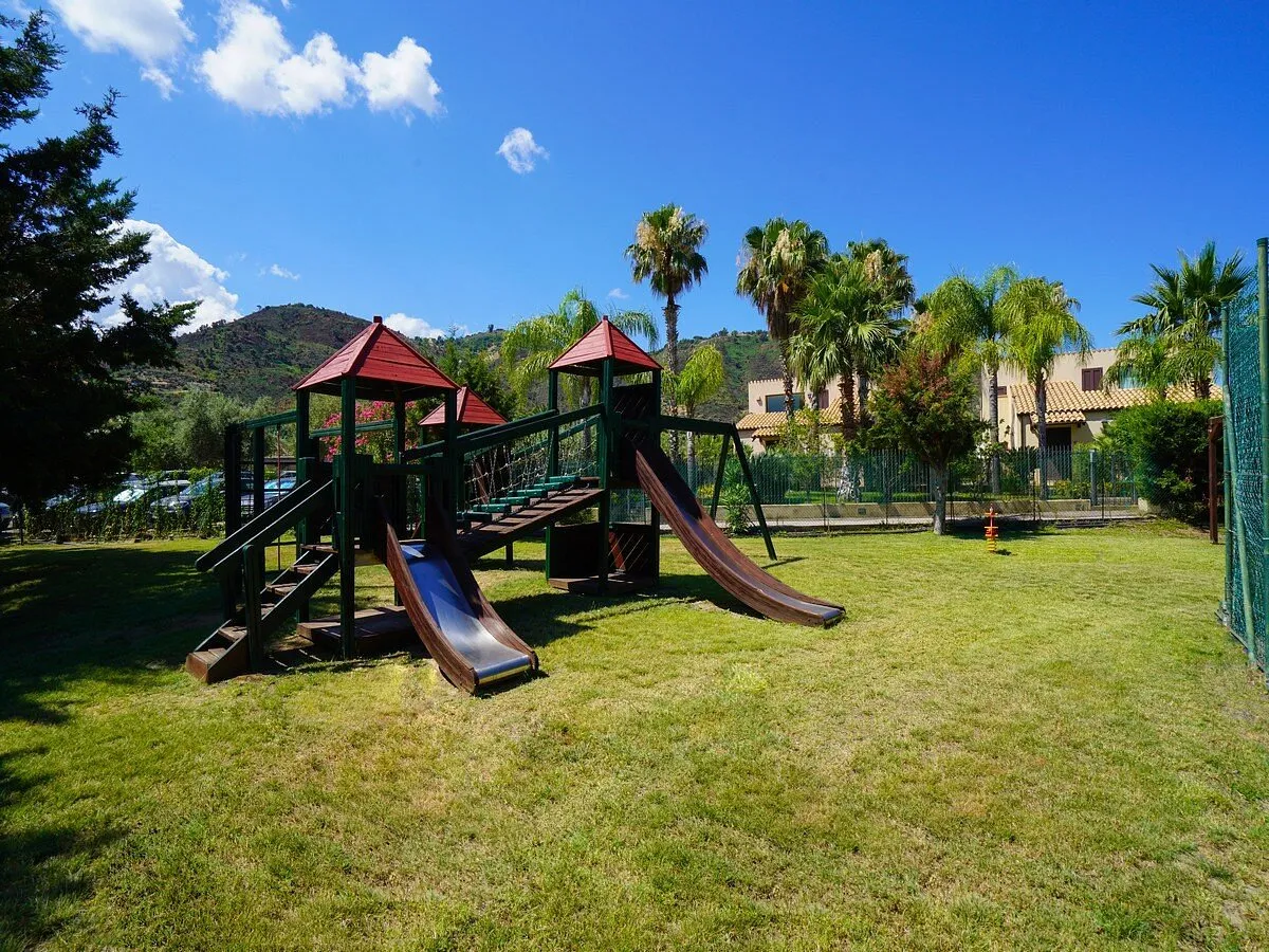 Parco giochi per bambini con scivoli su prato verde e palme