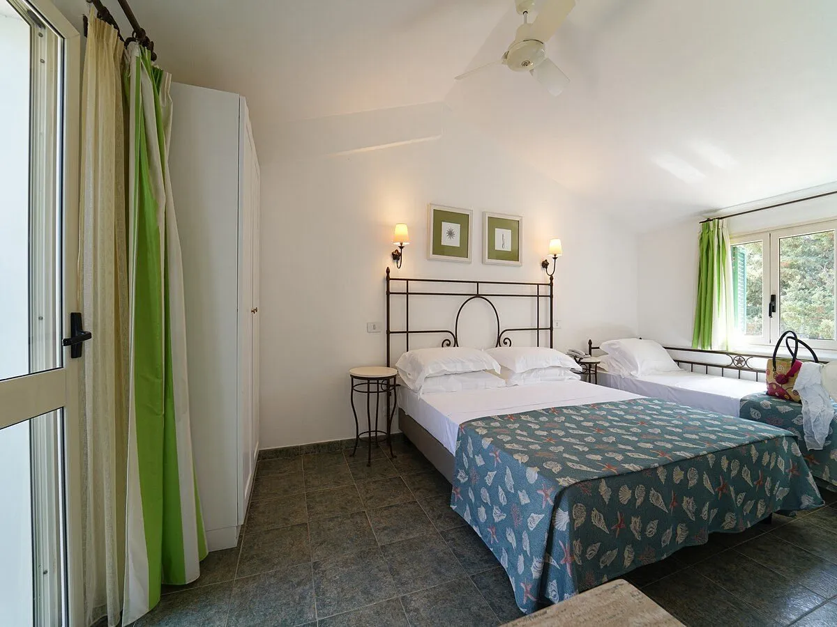 Camera con letto matrimoniale e singolo, tende verdi e ventilatore