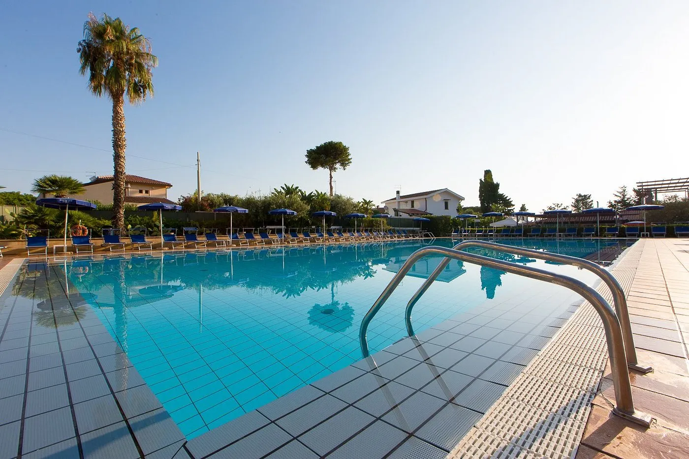 Piscina con acqua azzurra, lettini blu e palme al tramonto