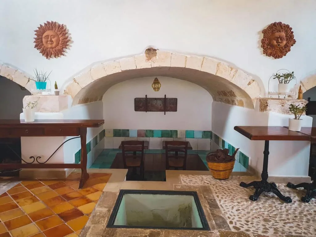 Sala interna in pietra con archi, decorazioni a forma di sole e pavimento in maioliche colorate