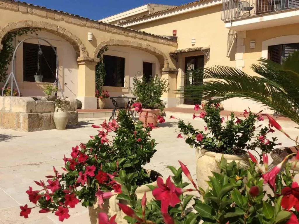 Cortile interno con archi in pietra, palme e fioriere di mandevilla rosa su pavimento chiaro