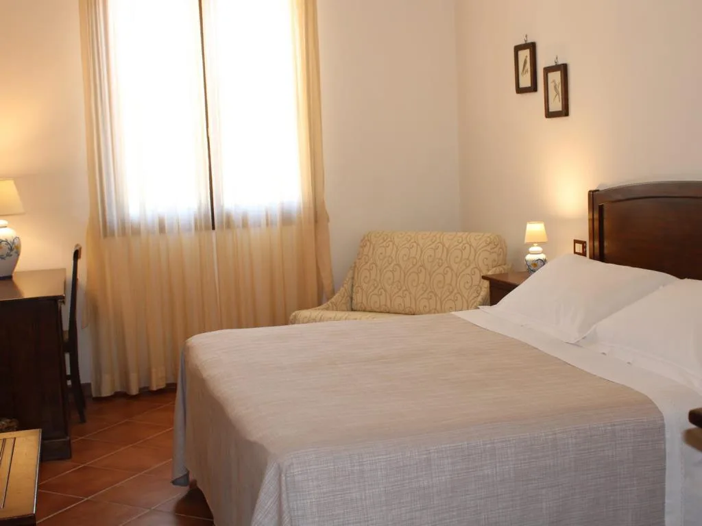 Camera da letto accogliente con letto matrimoniale, poltrona, comodini in legno e lampade in ceramica