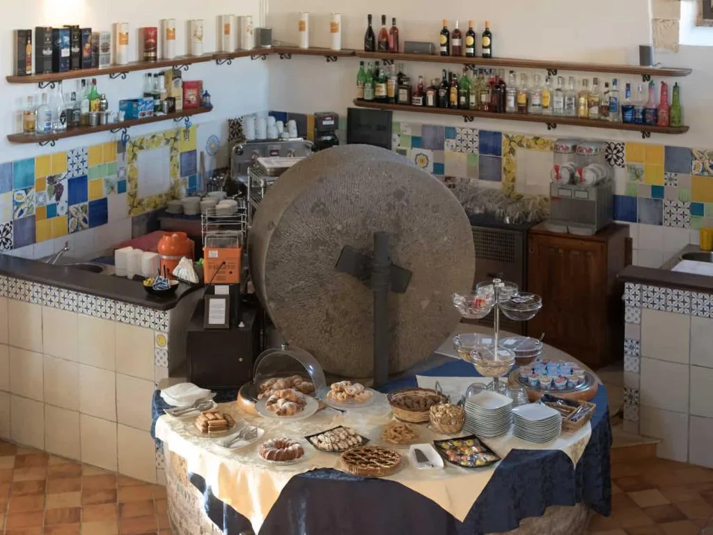 Angolo colazione con buffet di dolci e cornetti, antica macina in pietra e pareti decorate con maioliche