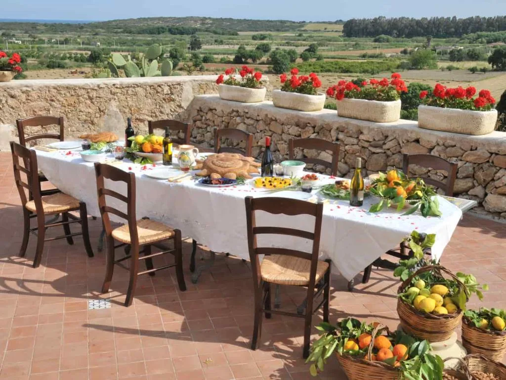 Tavolata all'aperto apparecchiata con prodotti tipici siciliani, cesti di agrumi e vista sulla campagna
