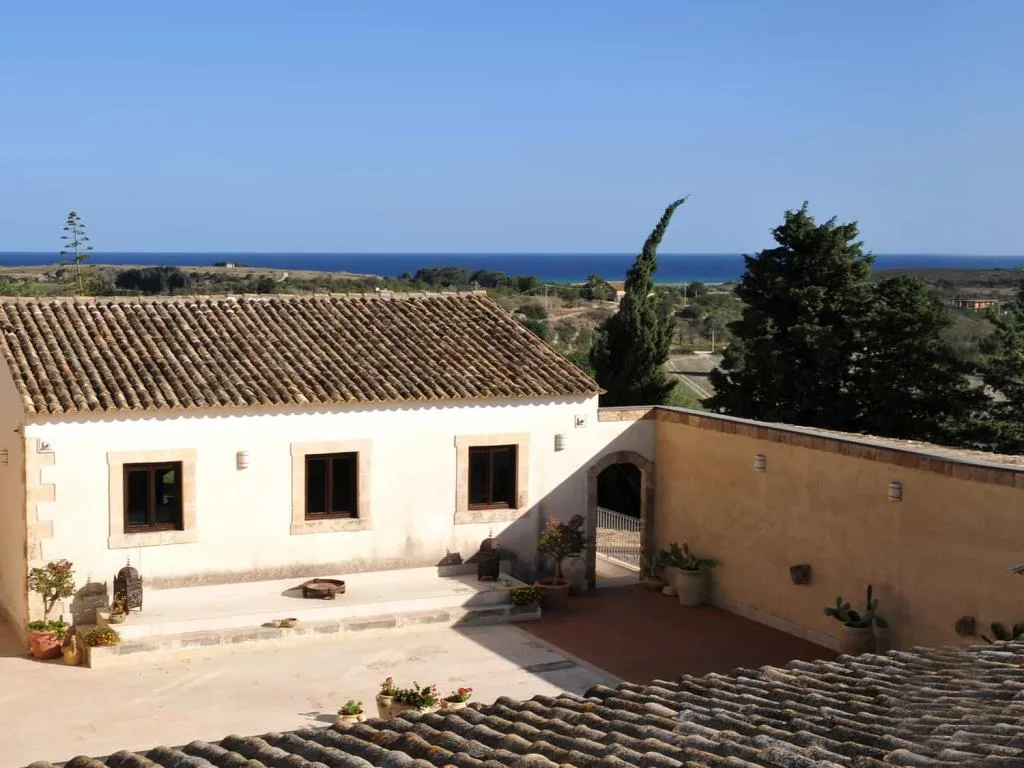Cortile con edificio rustico, tetto in tegole e affaccio sulla campagna e sul mare sullo sfondo