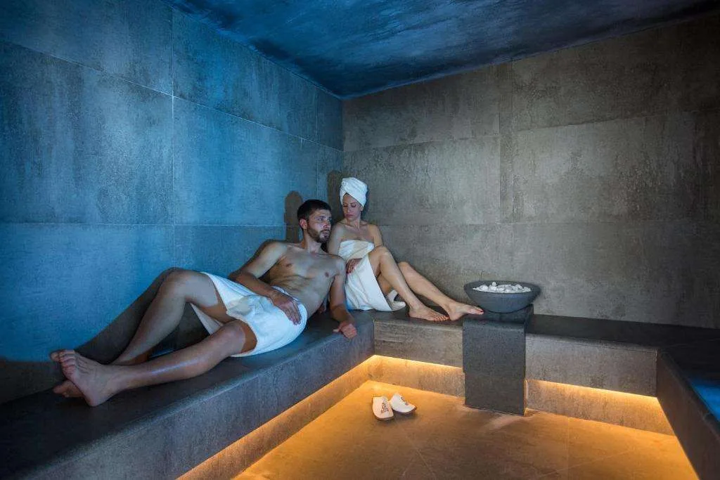 Bagno turco moderno in pietra grigia con coppia rilassata e illuminazione soffusa