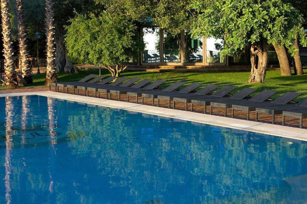 Piscina all'aperto con fila di lettini e alberi nel giardino
