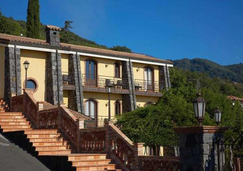 Facciata gialla dell'hotel con balconi in pietra circondata da colline