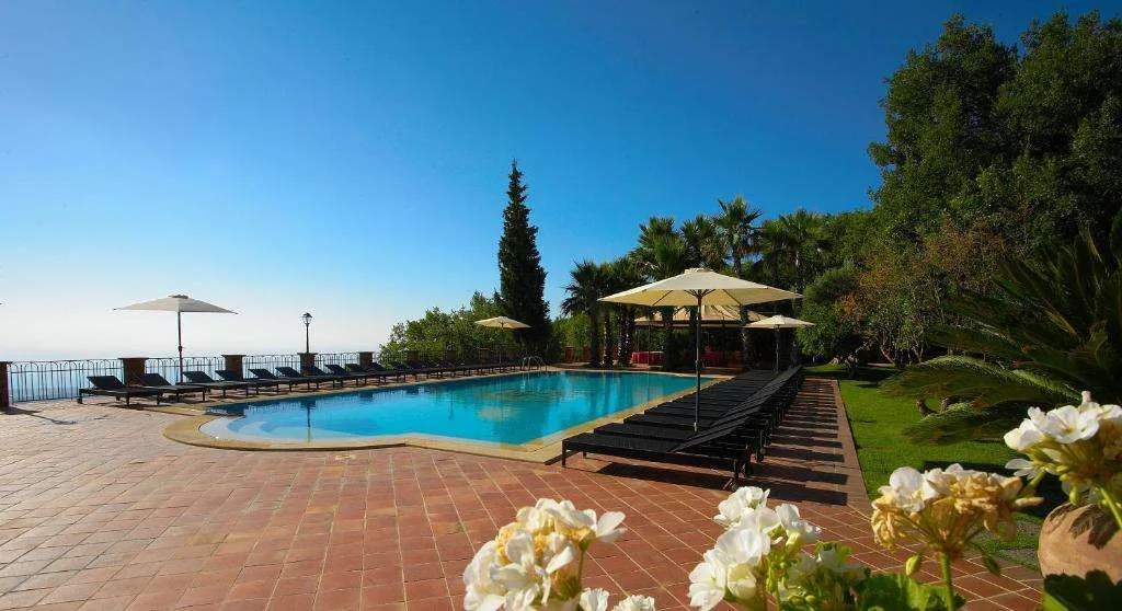 Piscina all'aperto con lettini, ombrelloni e vista sul mare e giardino
