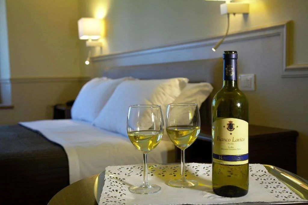 Dettaglio camera con due calici di vino bianco e bottiglia su vassoio