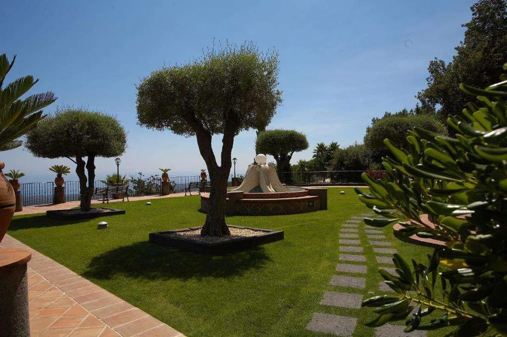 Giardino curato con prato, ulivi e fontana affacciato sul mare