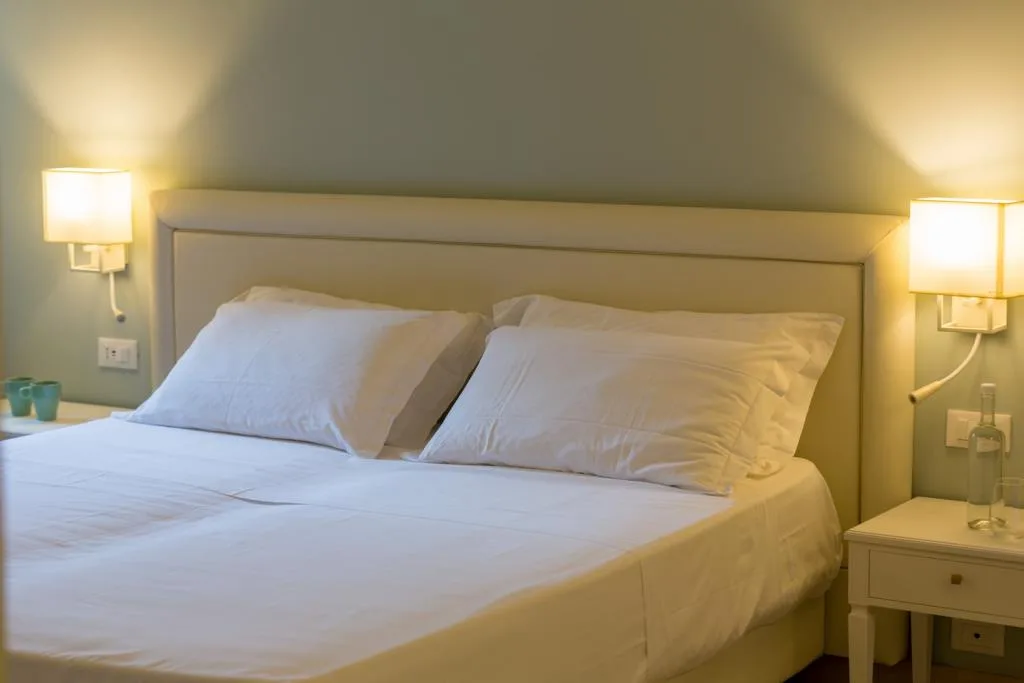 Testiera di letto con cuscini bianchi e lampade da parete