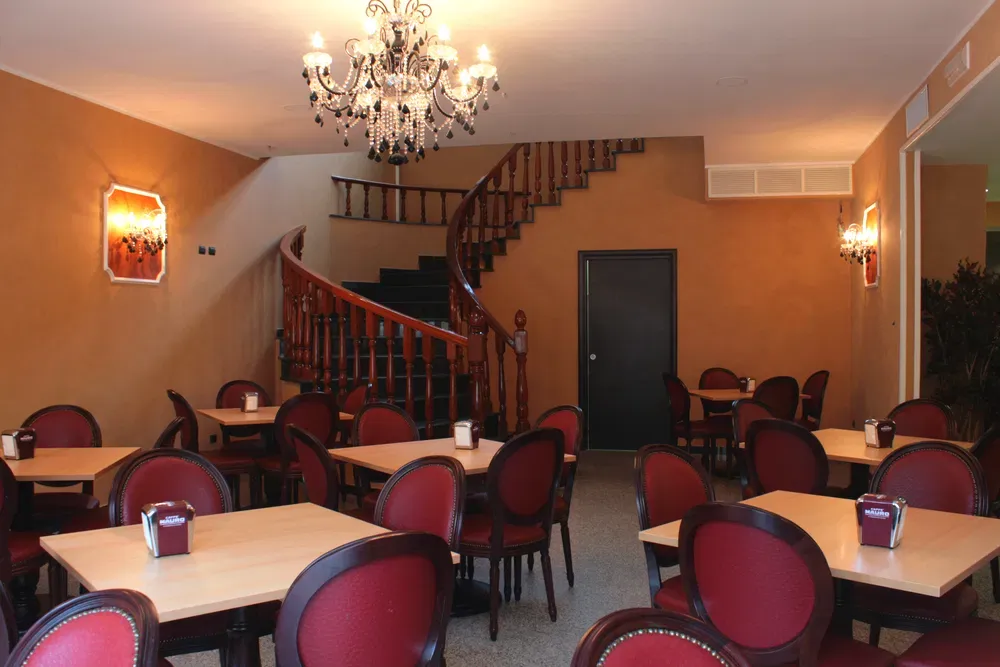 Sala ristorante con tavoli, sedie rosse, lampadario di cristallo e scala a chiocciola in legno