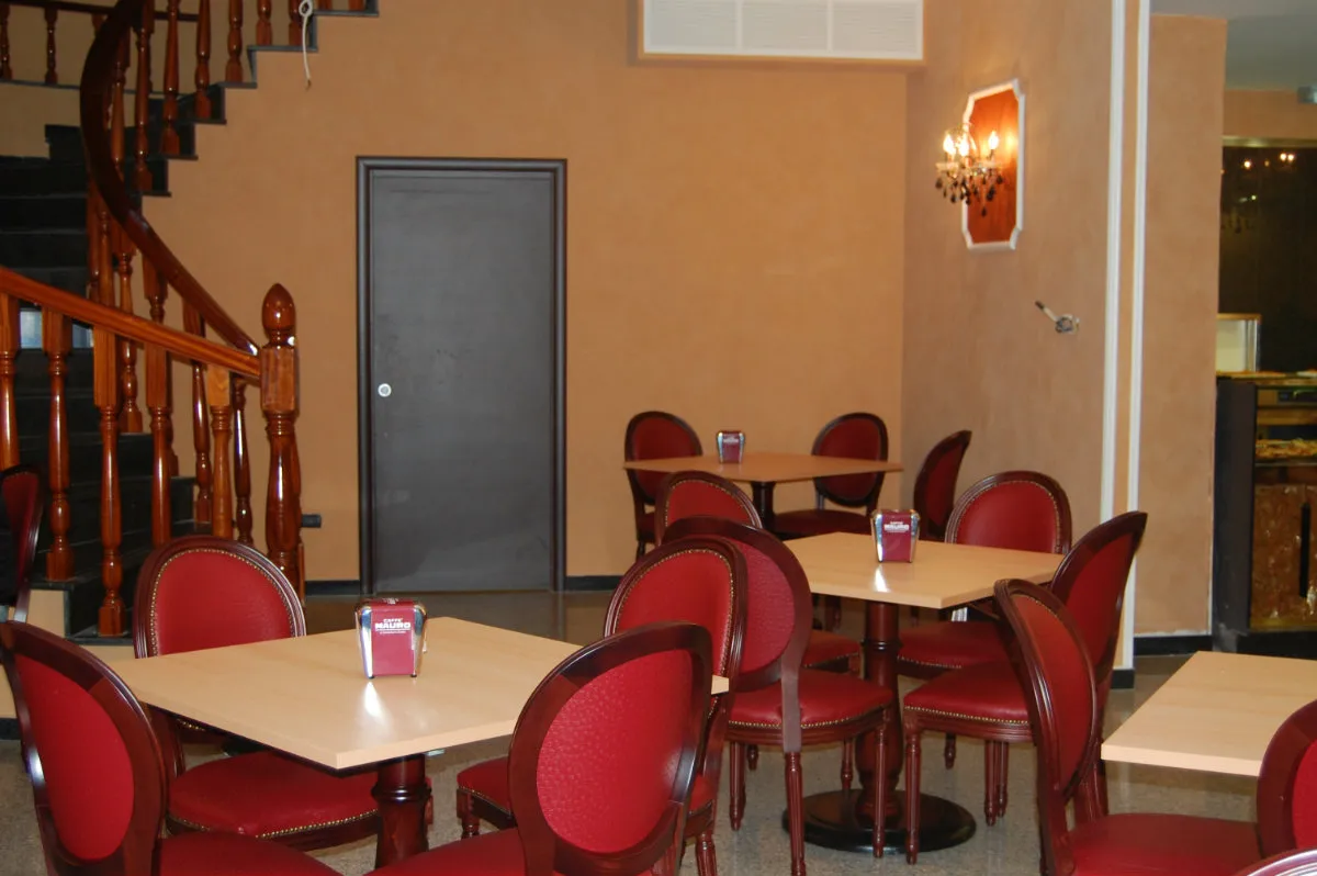 Sala ristorante con tavoli in legno chiaro, sedie rosse e scala interna in legno