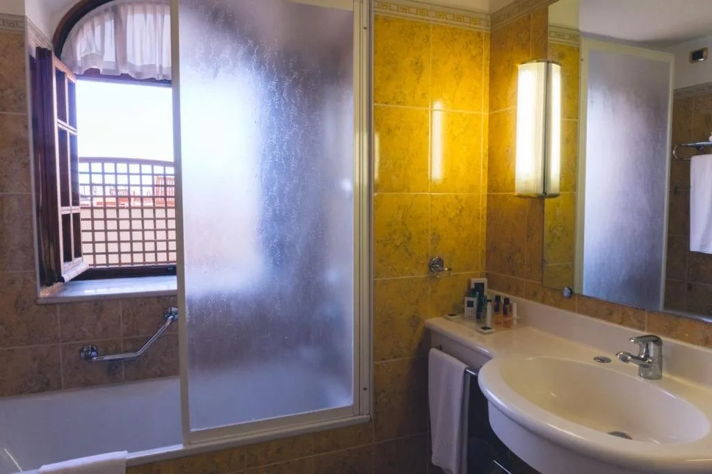 Bagno con piastrelle gialle, vasca con box doccia e finestra con vista sulla terrazza