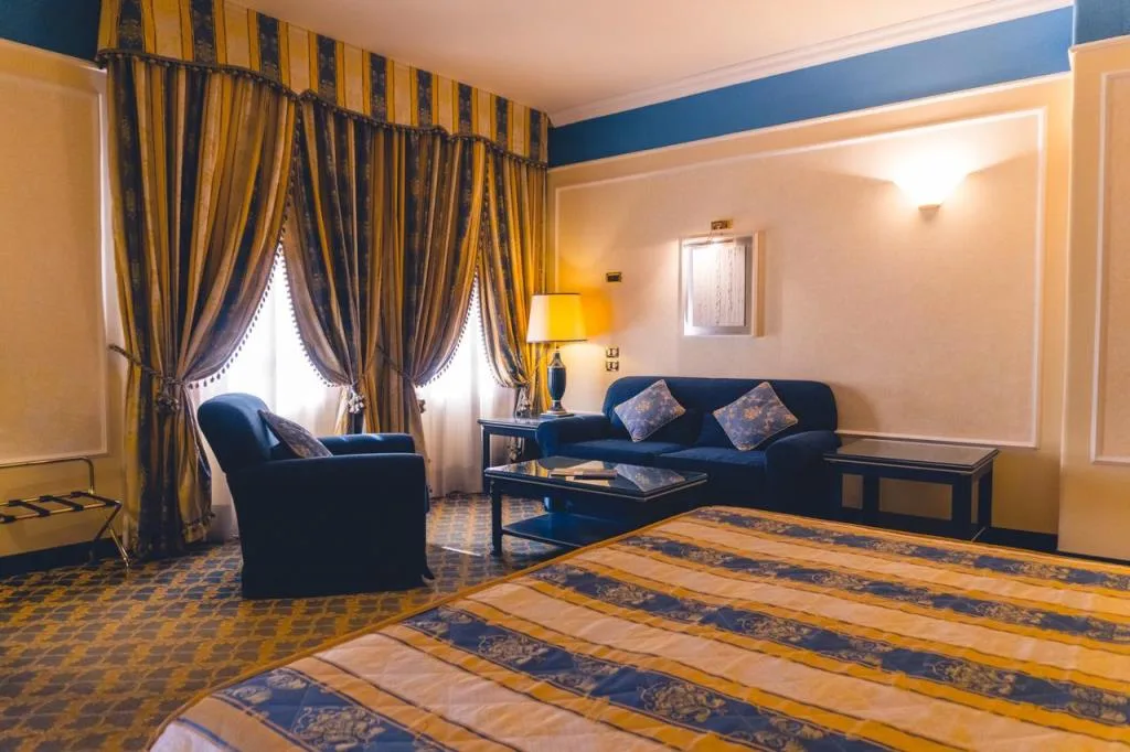 Camera con divano blu, tende a righe dorate e letto in primo piano