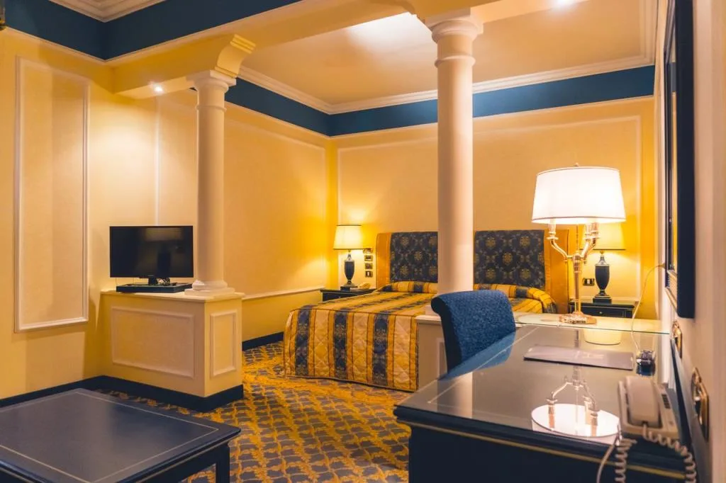 Camera elegante con colonne bianche, pareti gialle e letto con tessuti blu e oro