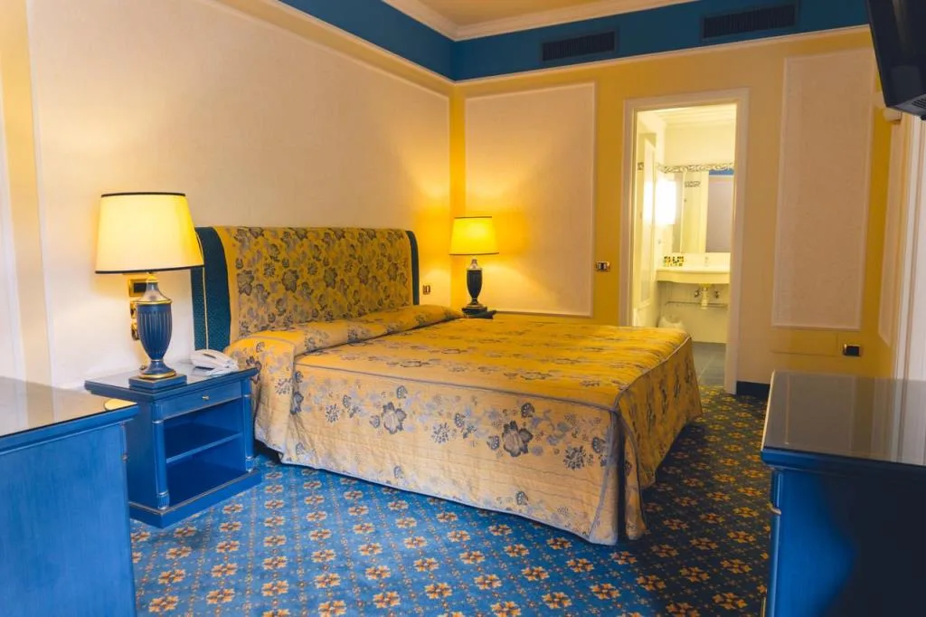 Camera con letto matrimoniale color giallo floreale, comodini blu e bagno adiacente