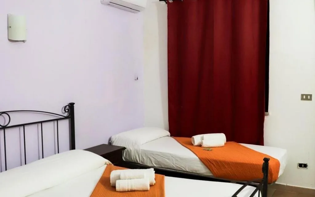 Camera con due letti singoli, biancheria bianca e arancione e tende rosse