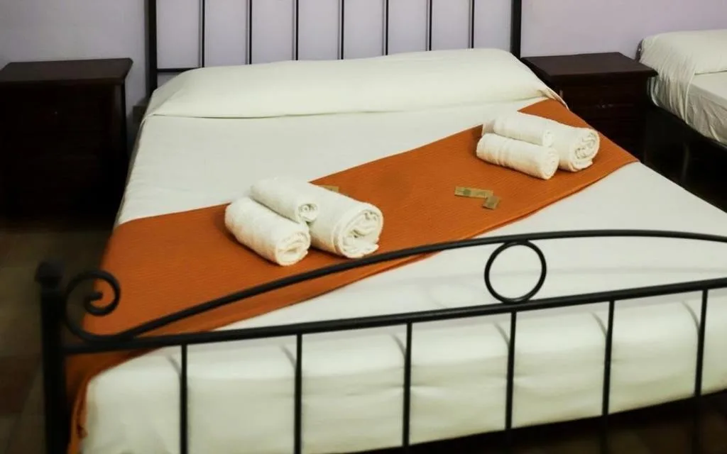 Letto matrimoniale con biancheria bianca e arancione e asciugamani arrotolati