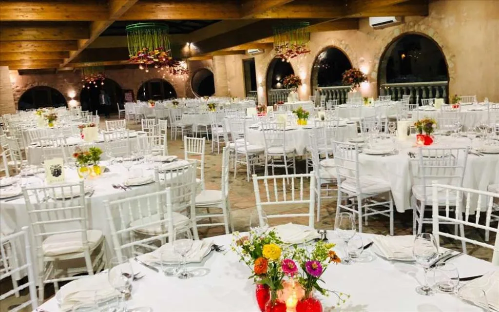 Sala ricevimenti allestita per evento con tavoli rotondi, tovaglie bianche e fiori