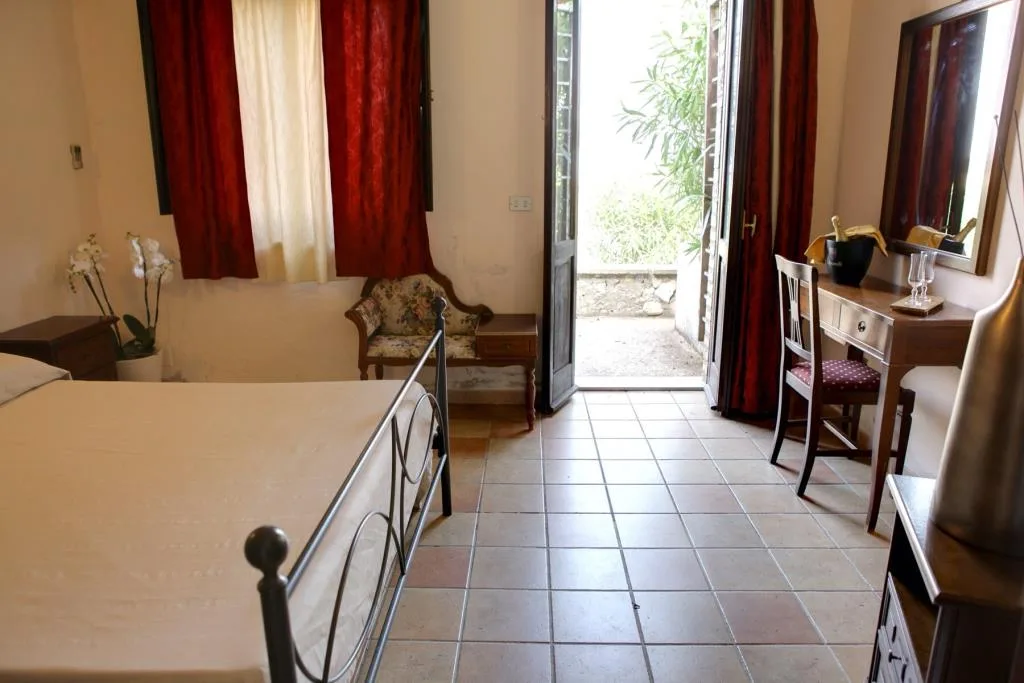 Camera con letto in ferro battuto, tende rosse e porta finestra sul giardino