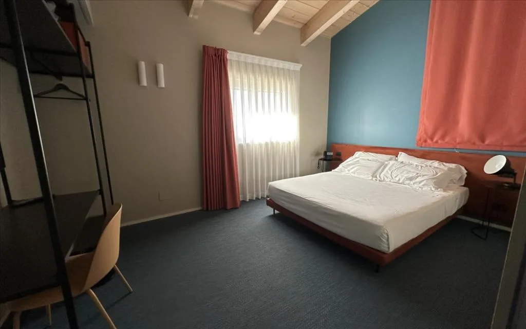 Camera con moquette blu, letto matrimoniale, parete azzurra e tende coordinate