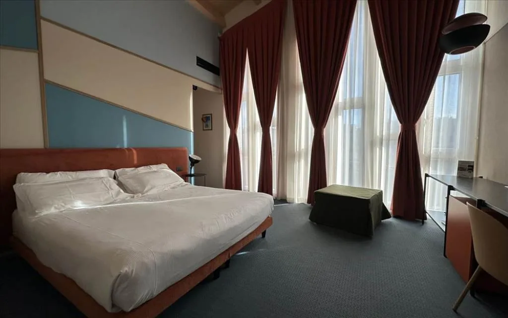 Camera con letto matrimoniale, grandi finestre con tende bordeaux e scrivania