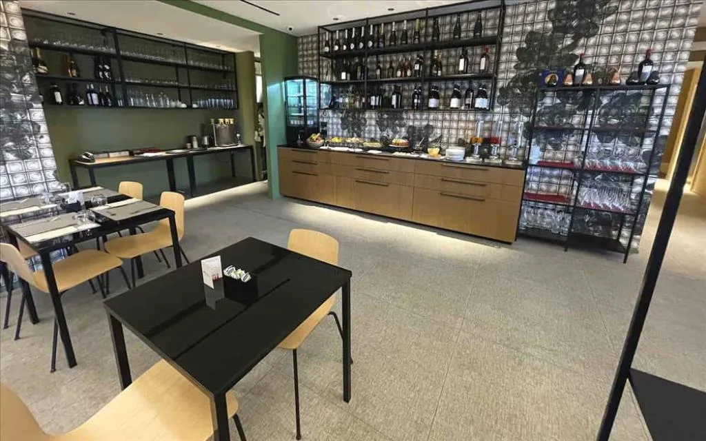 Sala colazione con buffet, mensole di bottiglie di vino e tavoli con sedie in legno