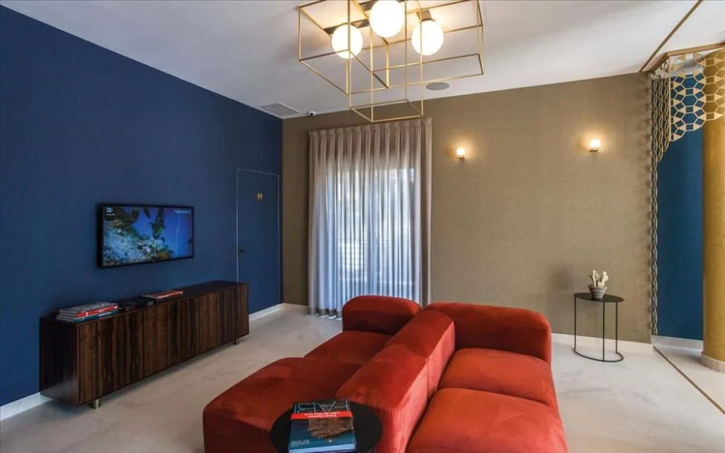 Salottino con divano rosso, parete blu, TV e lampadario dorato geometrico