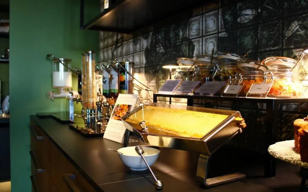 Buffet della colazione con dispenser di cereali, torte e marmellate su parete piastrellata