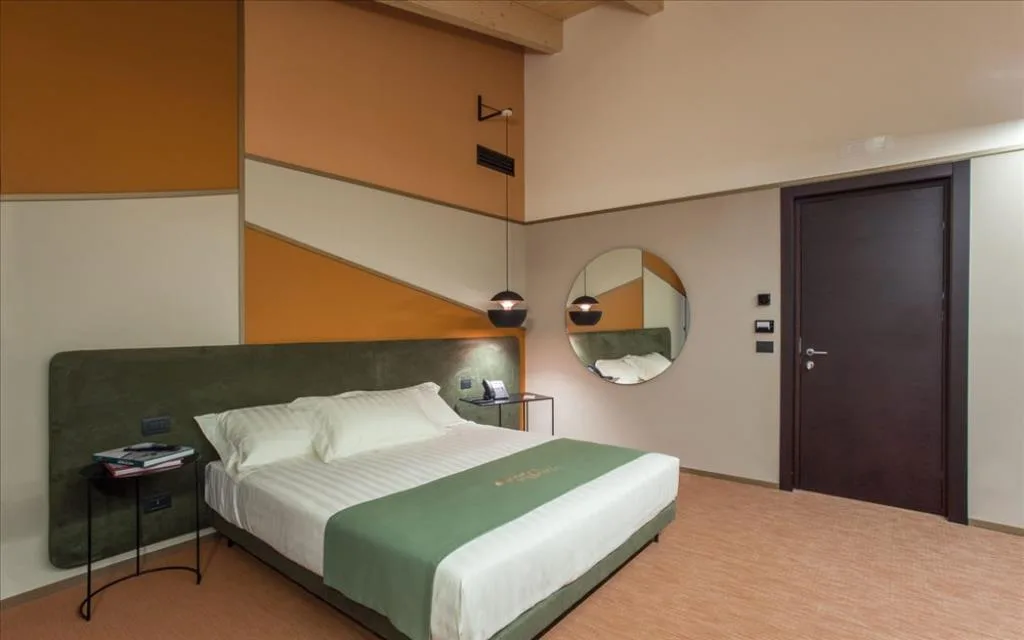 Camera elegante con letto matrimoniale, parete geometrica arancione e specchio rotondo