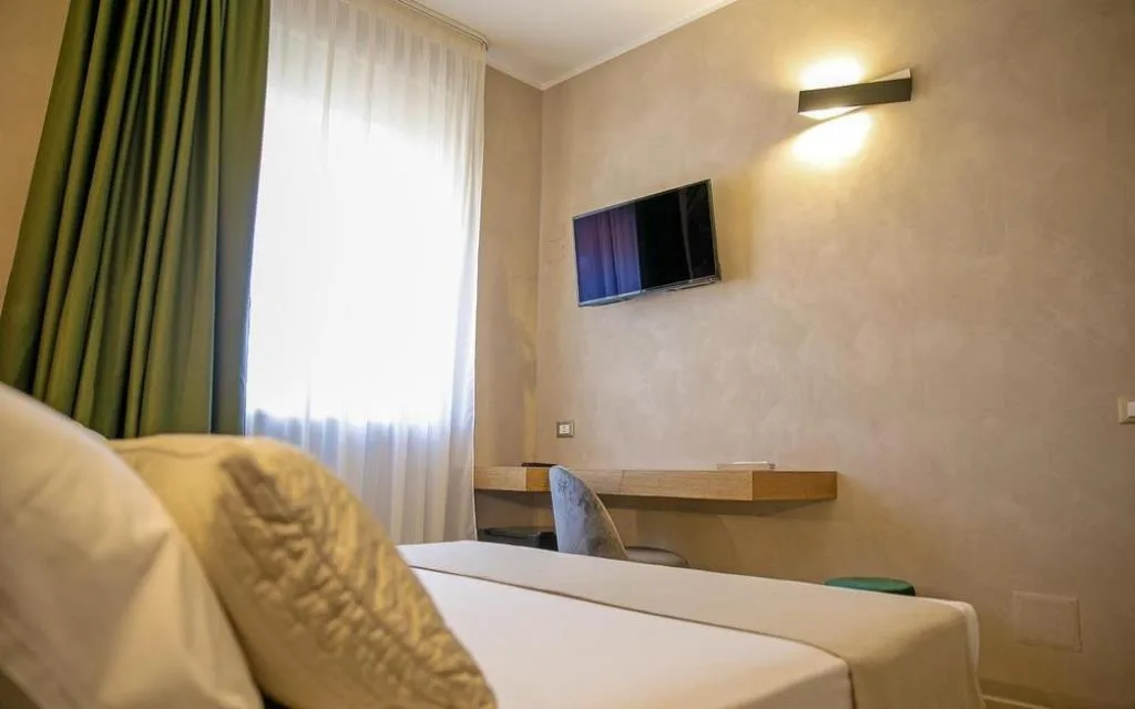 Camera moderna con testiera imbottita, scrivania in legno, TV a parete e tende verdi