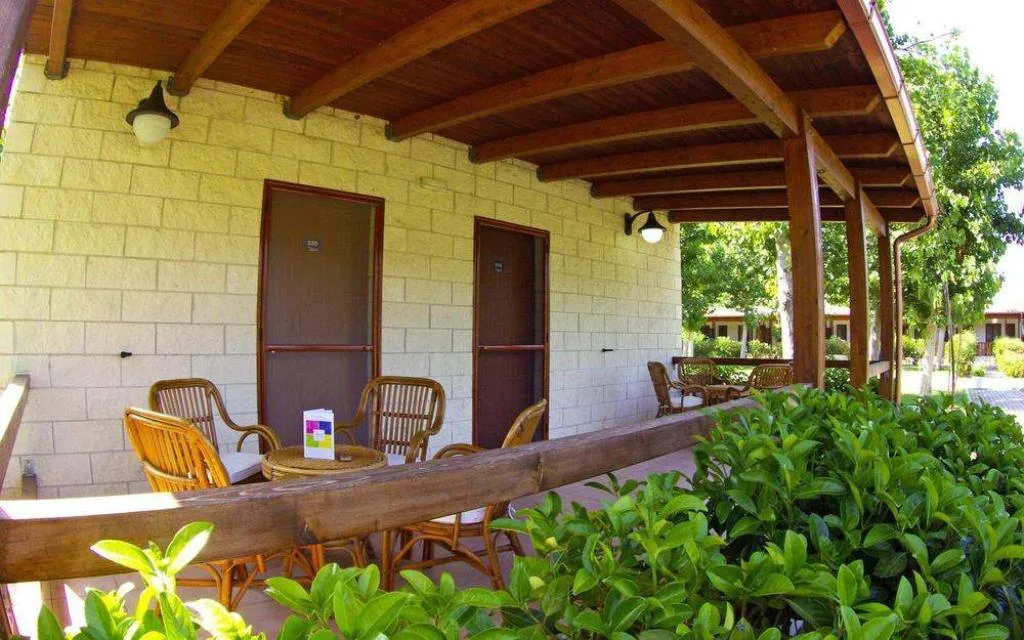 Portico esterno in legno con sedie in rattan e ingressi delle camere immersi nel verde
