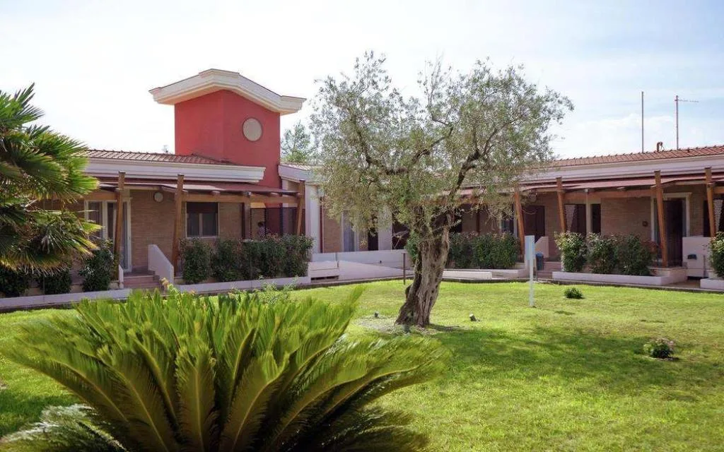 Cortile interno con prato verde, ulivo e struttura in mattoni con torretta rossa