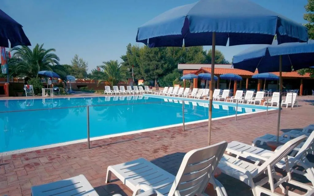 Piscina all'aperto con lettini bianchi e ombrelloni blu circondata dalla vegetazione