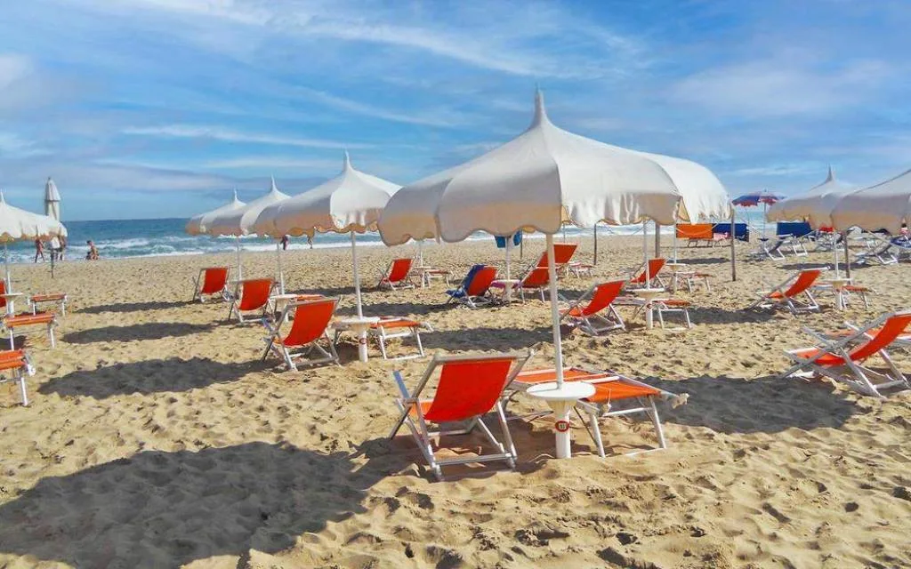 Spiaggia sabbiosa con ombrelloni bianchi e lettini arancioni vista mare