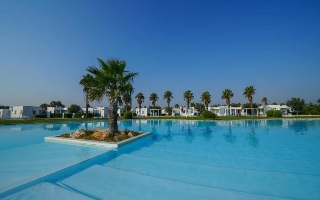 Piscina con isola centrale di palma e bungalow sullo sfondo