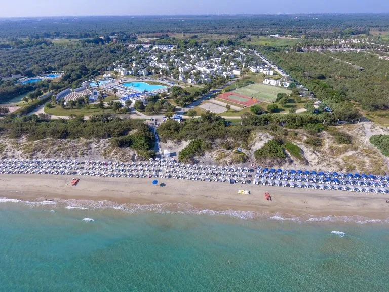 Vista aerea della spiaggia con ombrelloni e resort immerso nel verde
