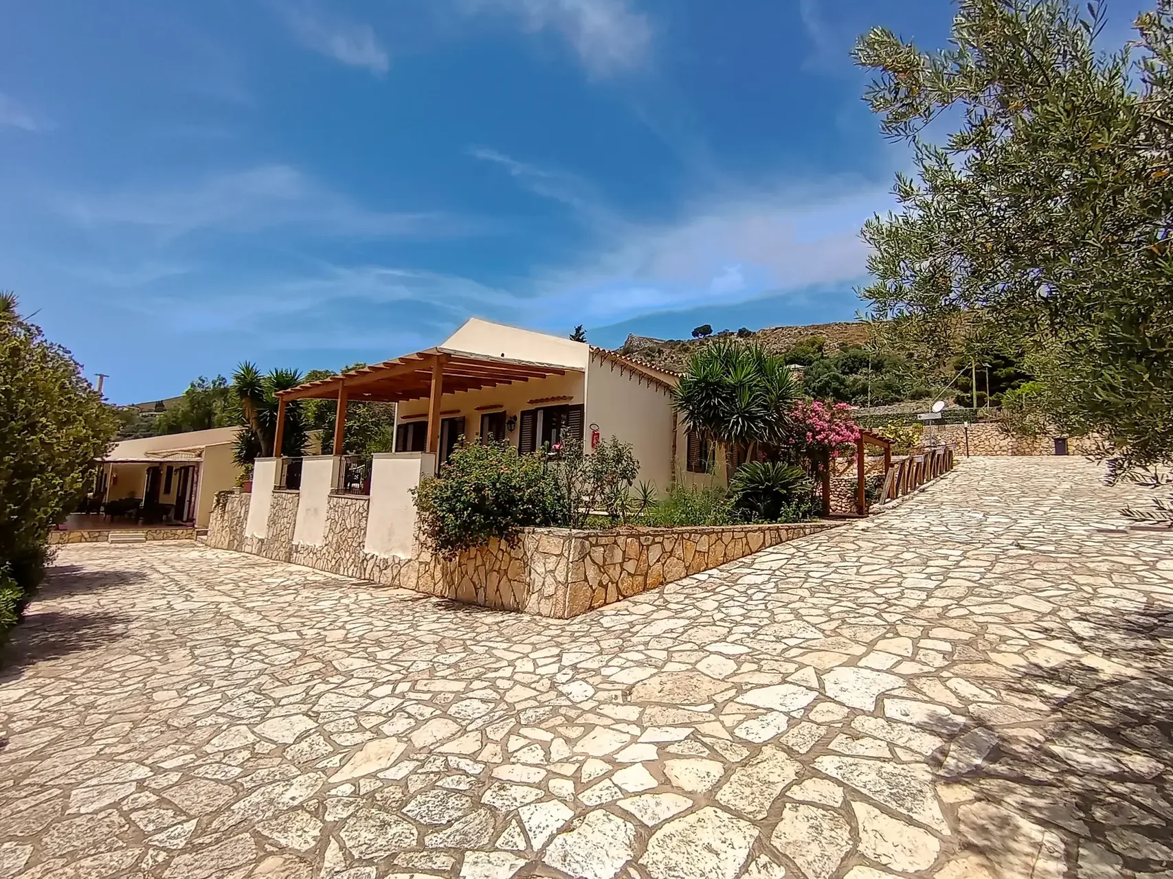 Vista esterna dell'hotel con pavimentazione in pietra, pergolato e giardino fiorito