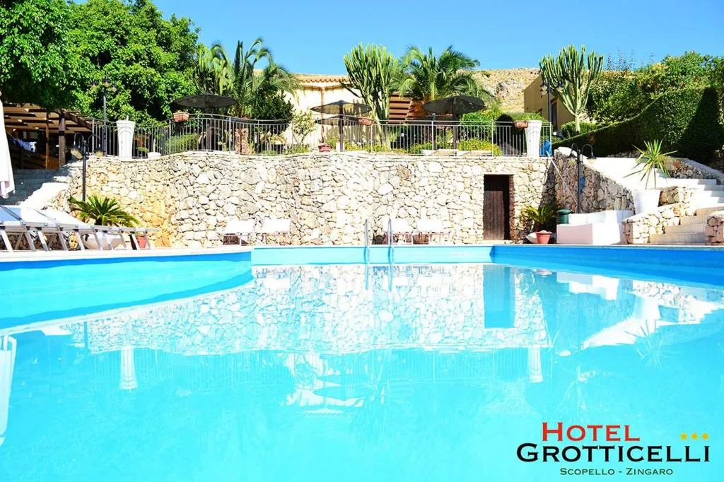 Piscina azzurra con muretto in pietra, palme e lettini al sole