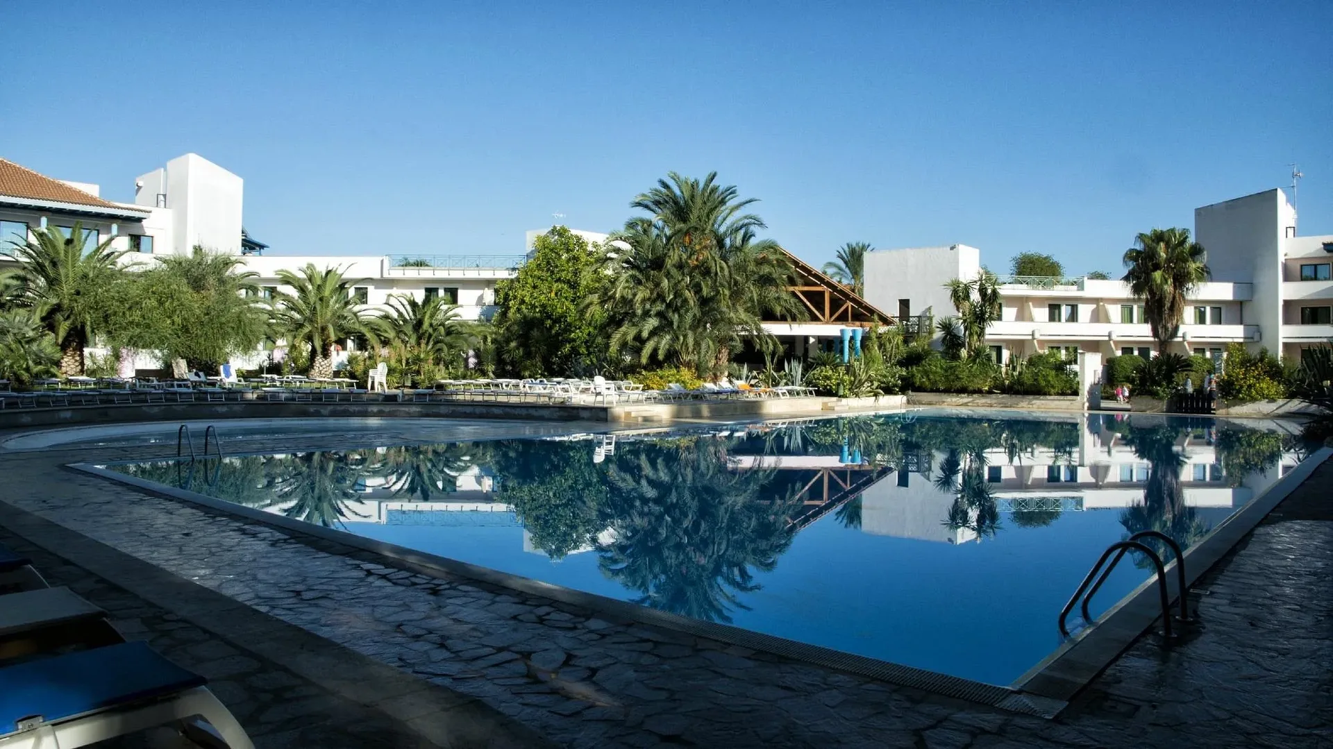 Piscina esterna con acqua limpida che riflette le palme e gli edifici del resort