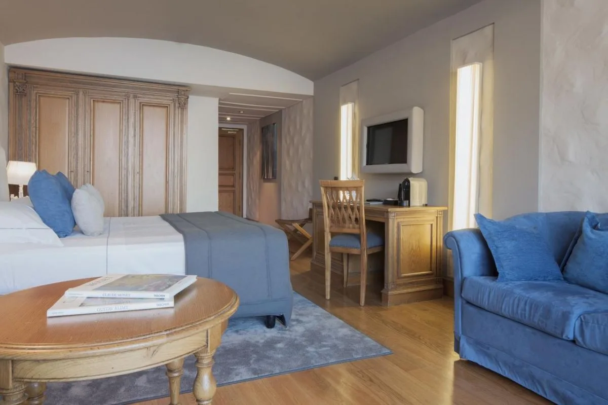 Camera spaziosa con letto, divano blu, scrivania e testiera in legno intagliato