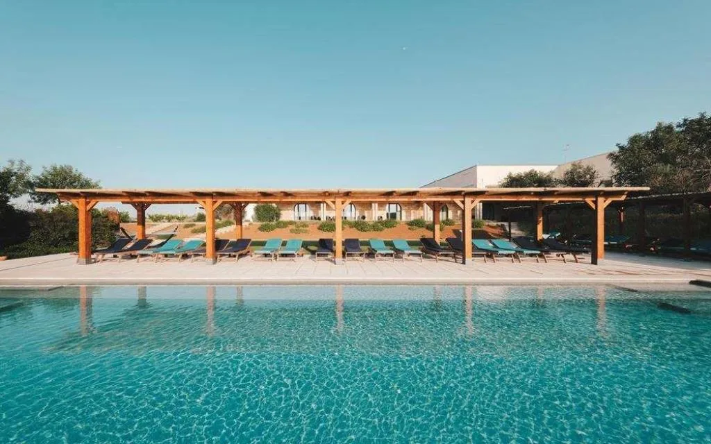 Piscina con lettini blu sotto lungo pergolato in legno e cielo azzurro