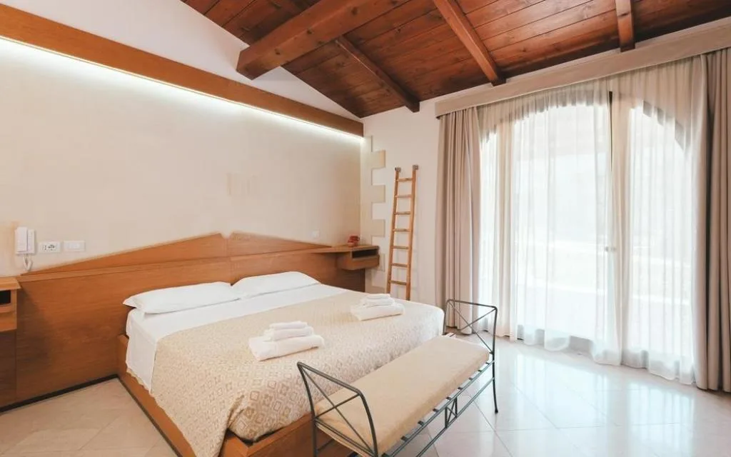 Camera matrimoniale con soffitto in legno a vista e ampia vetrata luminosa