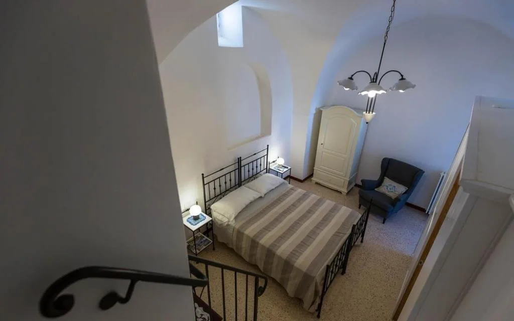 Camera con soffitto a volta bianco, letto in ferro battuto, poltrona blu e armadio bianco vista dall'alto
