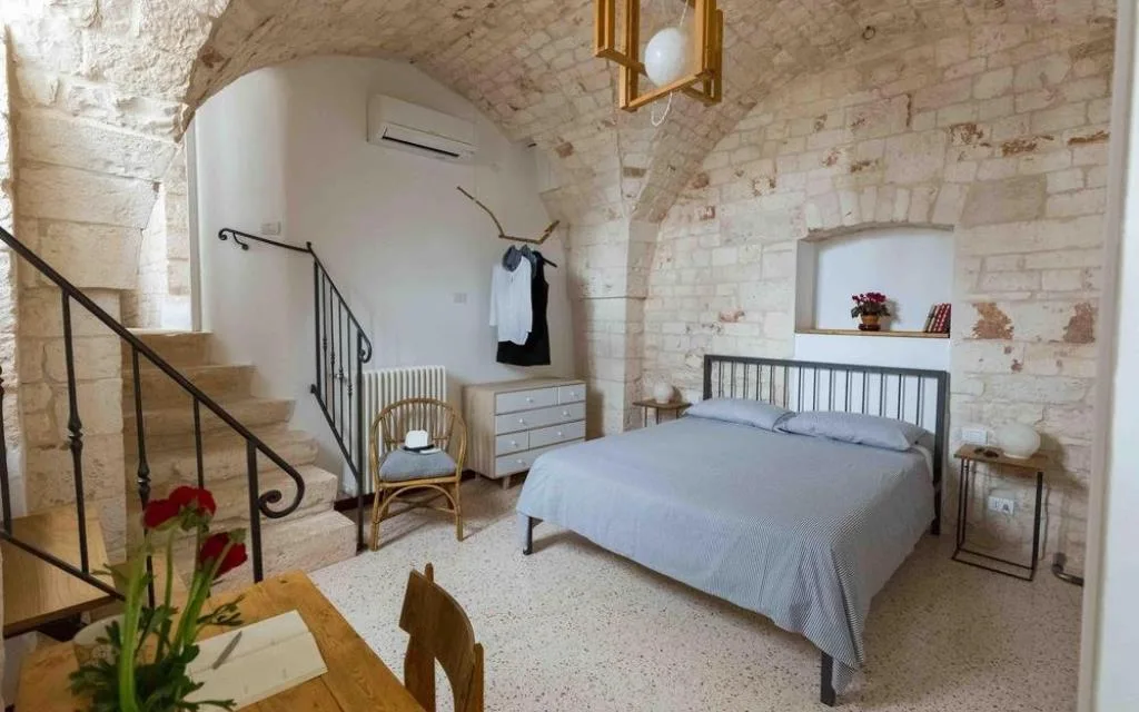 Ampia camera con soffitto a volta in pietra, letto matrimoniale, scala interna e area con tavolo in legno