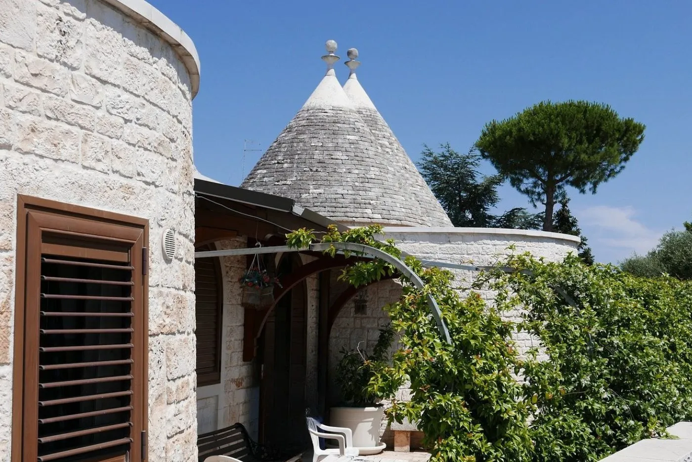 Trullo tradizionale con tetto conico in pietra, terrazza con vegetazione e cielo azzurro