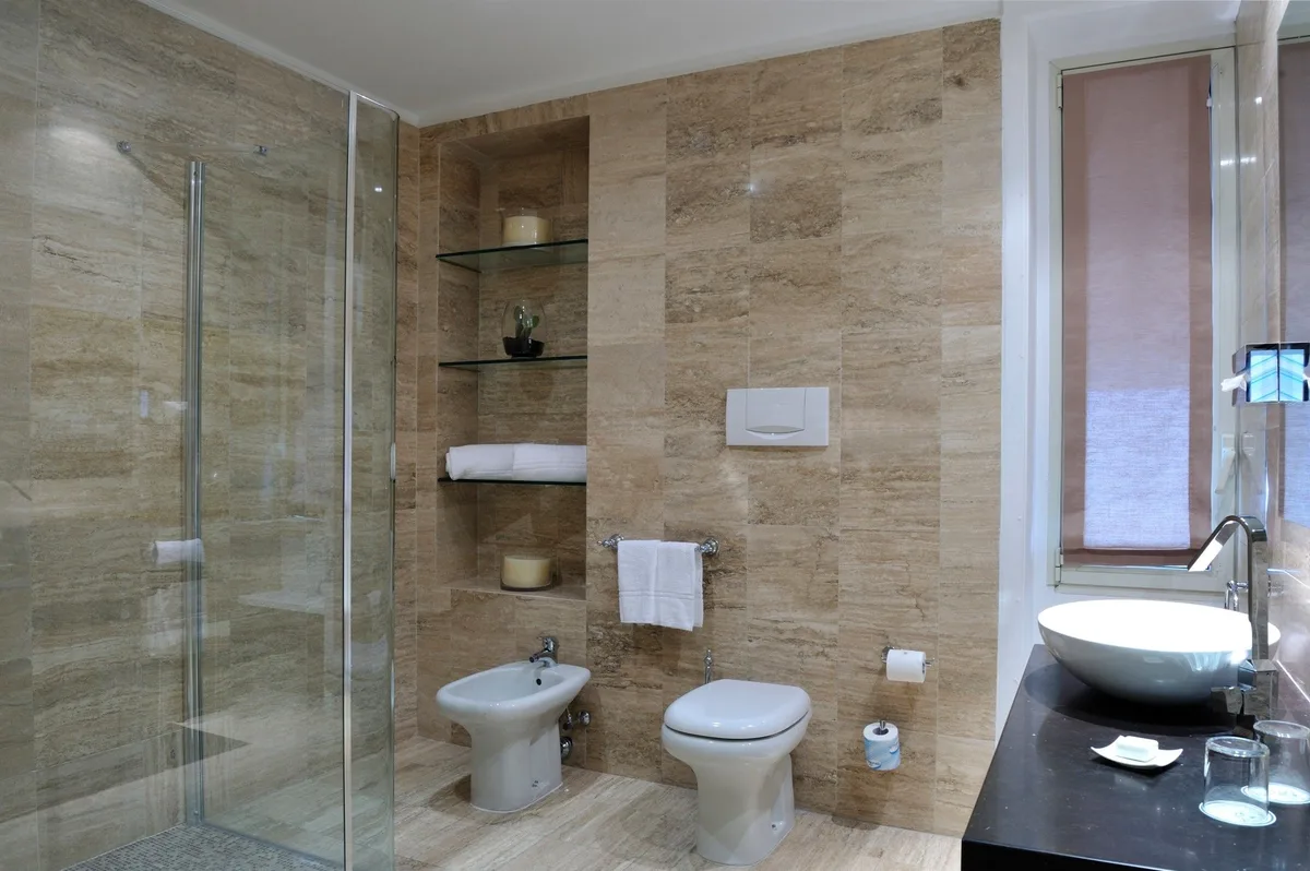 Bagno rivestito in travertino con doccia in vetro, bidet, wc e lavabo da appoggio